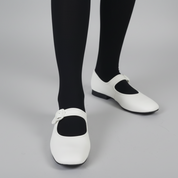 White shoes with a button detail worn with black socks on a dark floor.