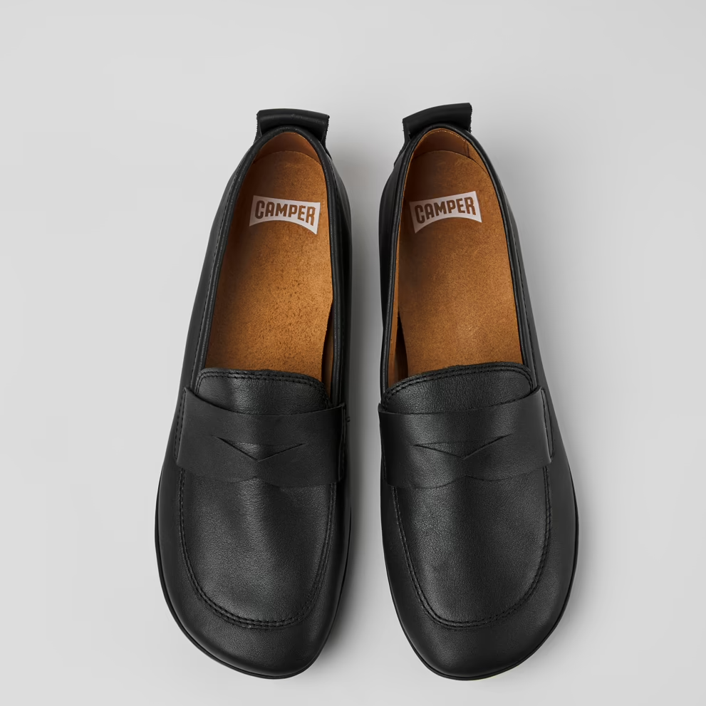 Pair of black leather loafer shoes with brown soles on a light gray background