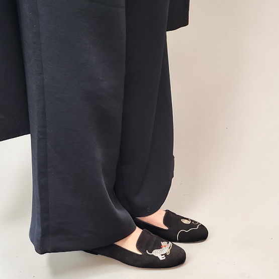 Person wearing black wide-leg pants and black shoes with white patterns on a beige background