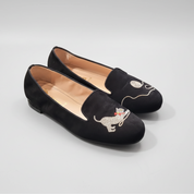 Black loafers with dog embroidery on a light gray surface
