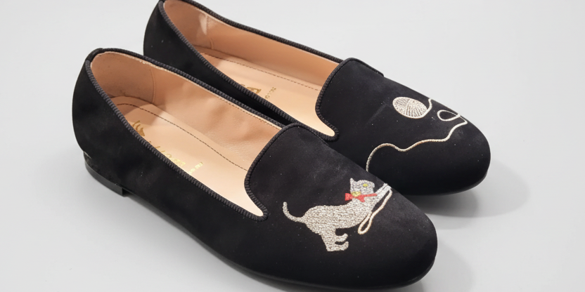 Black loafers with dog embroidery on a light gray surface