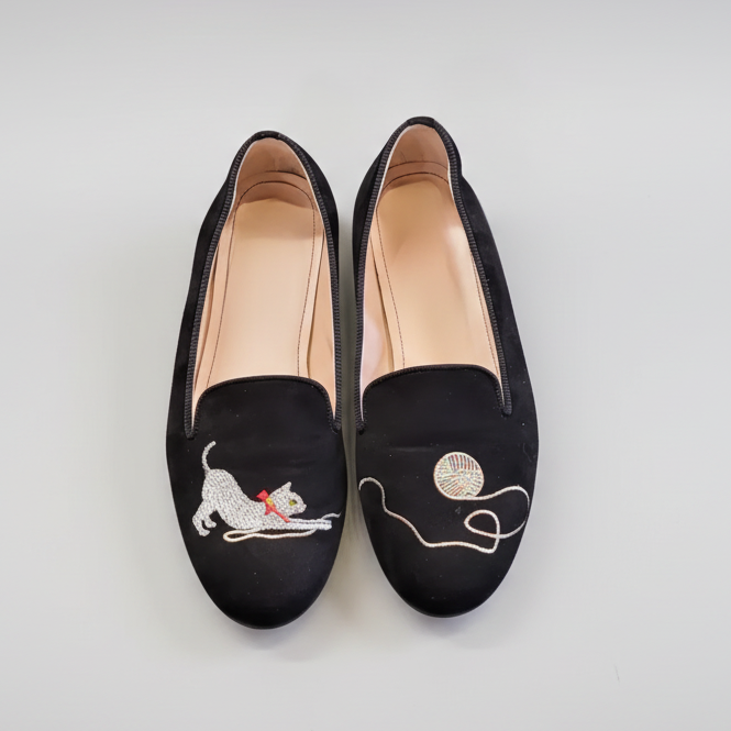 Black loafers with embroidered designs on a concrete surface