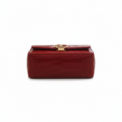 Red crocodile-patterned handbag with a gold clasp on a white background