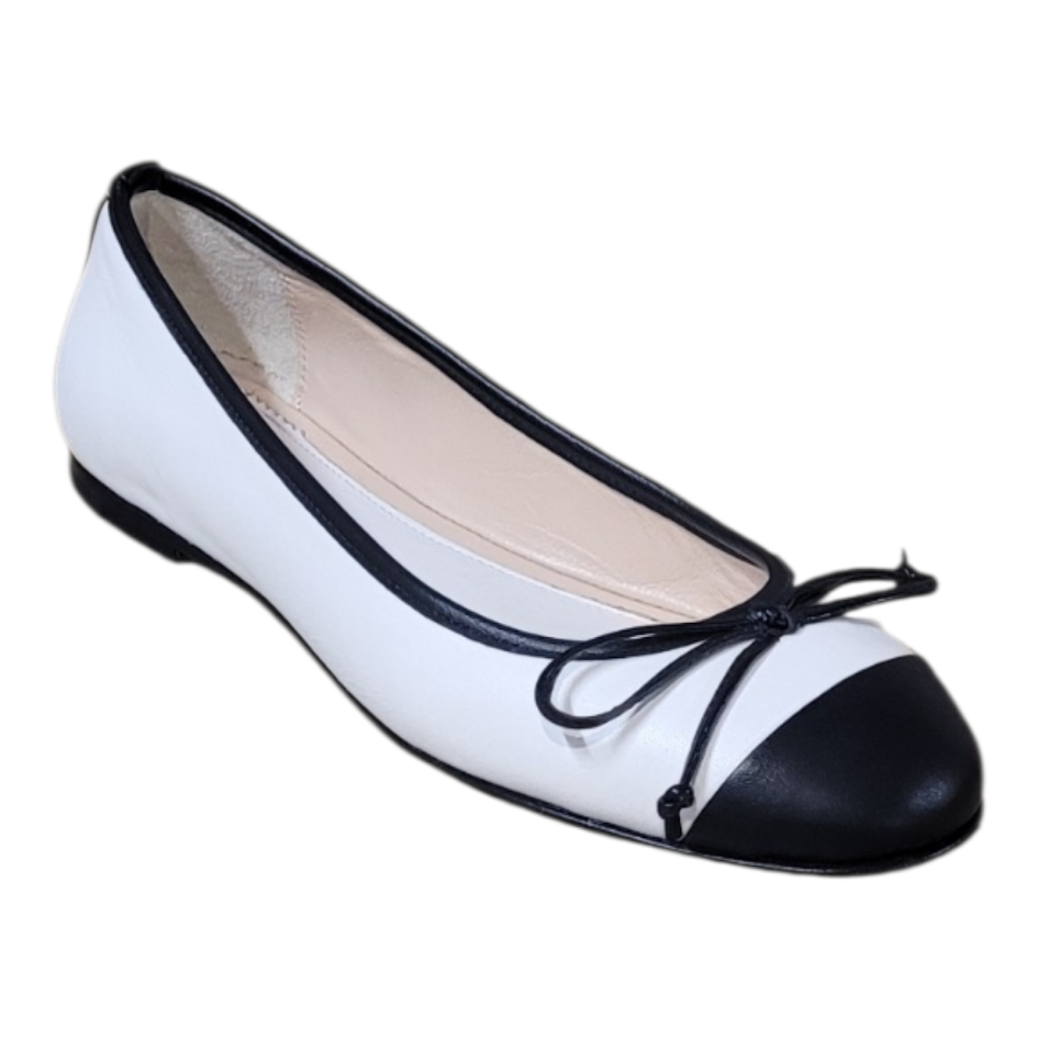 A white ballet flat shoe with a black toe cap and black trim, featuring a black ribbon bow on the front, shown against a plain white background.