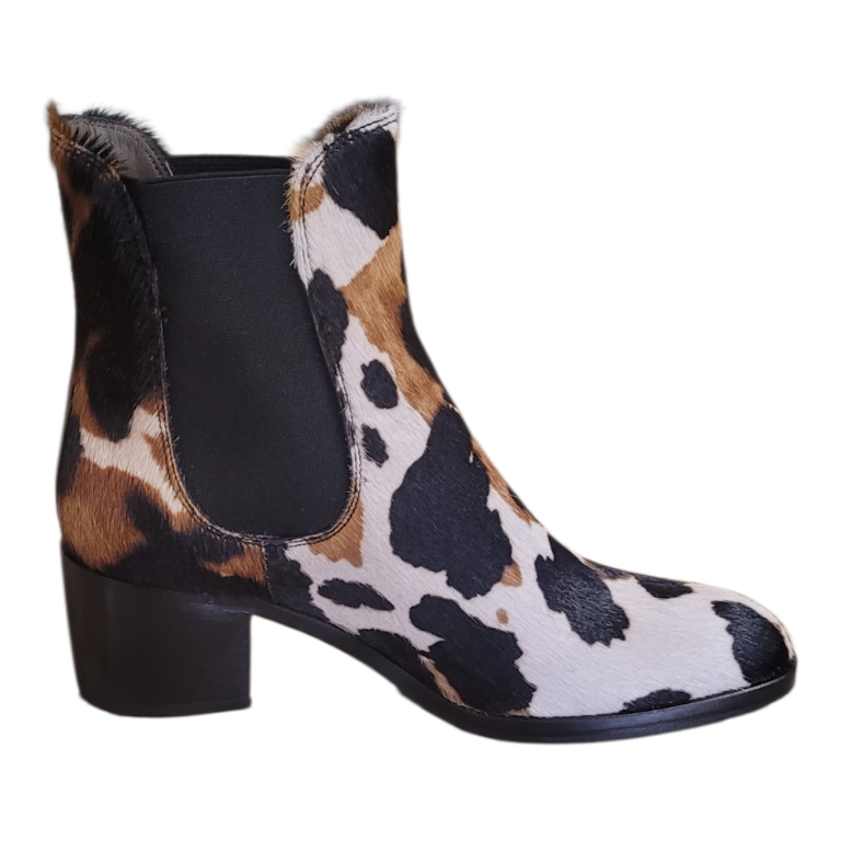 A single women's ankle boot with a black, brown, and beige cow-print pattern, featuring a black elastic side panel and a black block heel, shown against a plain white background.