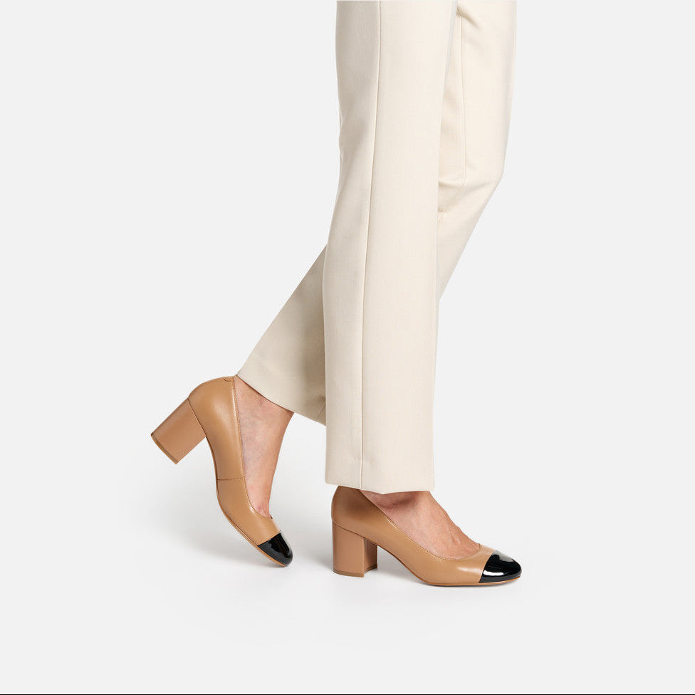 Tan high-heeled shoes with black accents worn with beige pants on a white background