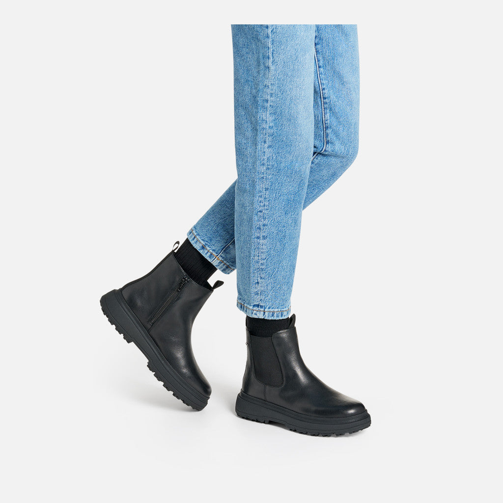 Black Chelsea boots worn with light blue jeans on a white background