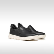 Black slip-on shoes with white soles on a light gray background