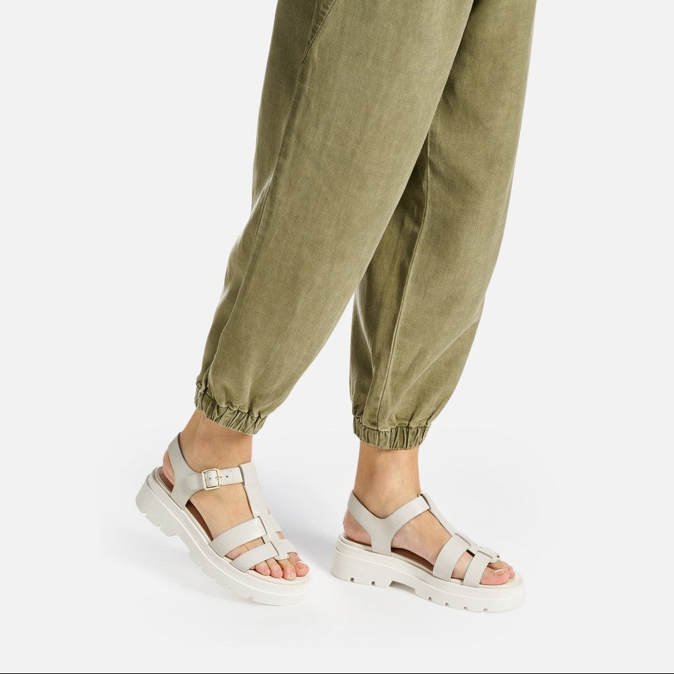 Person wearing cream sandals and green jogger pants on a white background