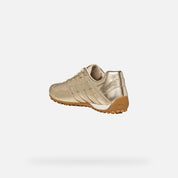 Gold sneaker with white sole on a light gray background