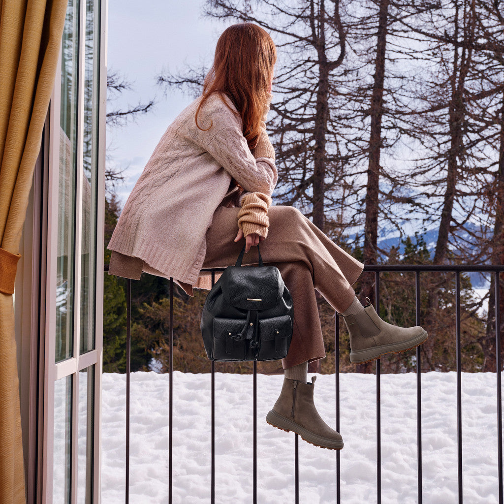 Person sitting on a railing with a snowy landscape and trees in the background