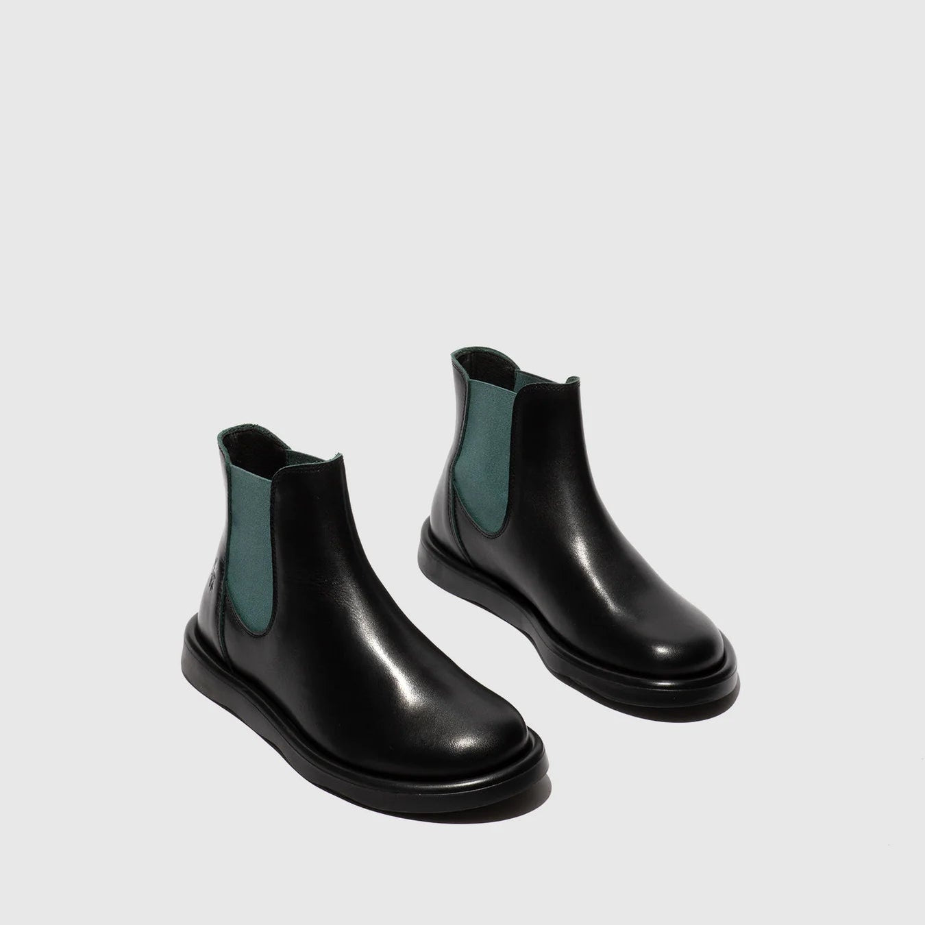 Pair of black Chelsea boots with green accents on a light gray background
