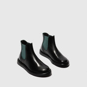 Pair of black Chelsea boots with green accents on a light gray background