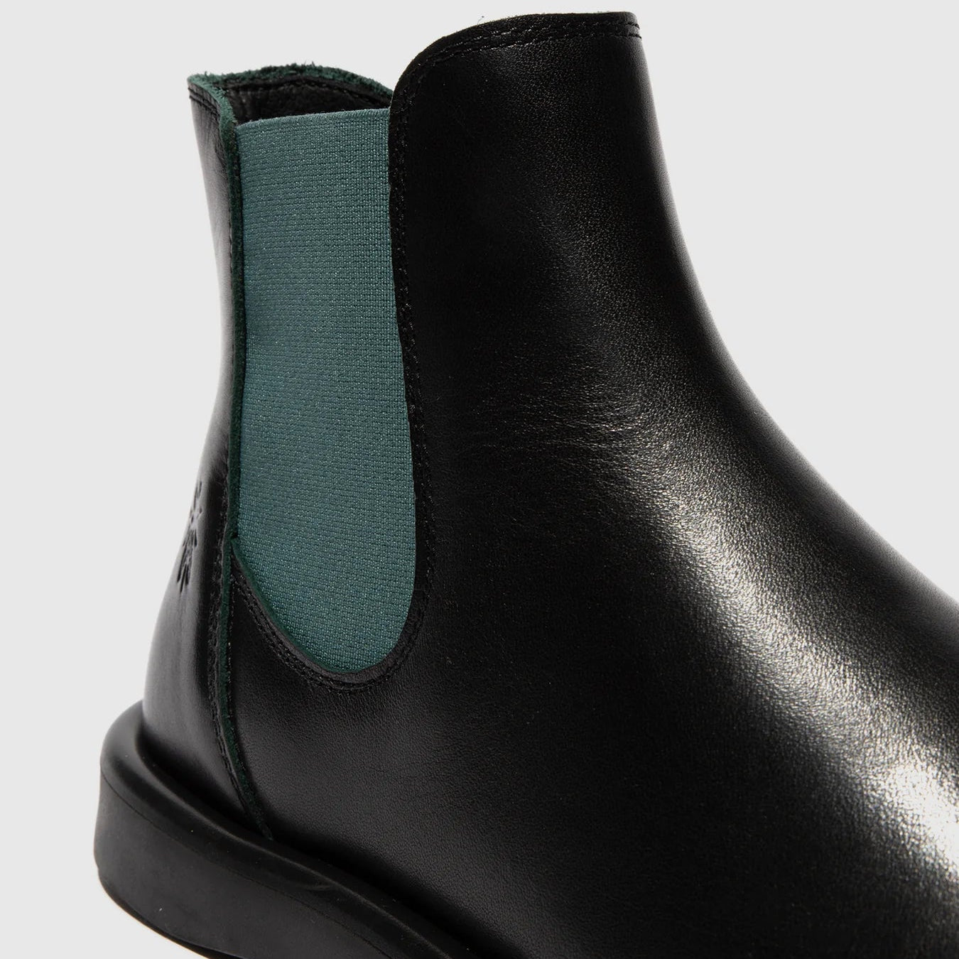Black Chelsea boot with green elastic side tab on a light gray background
