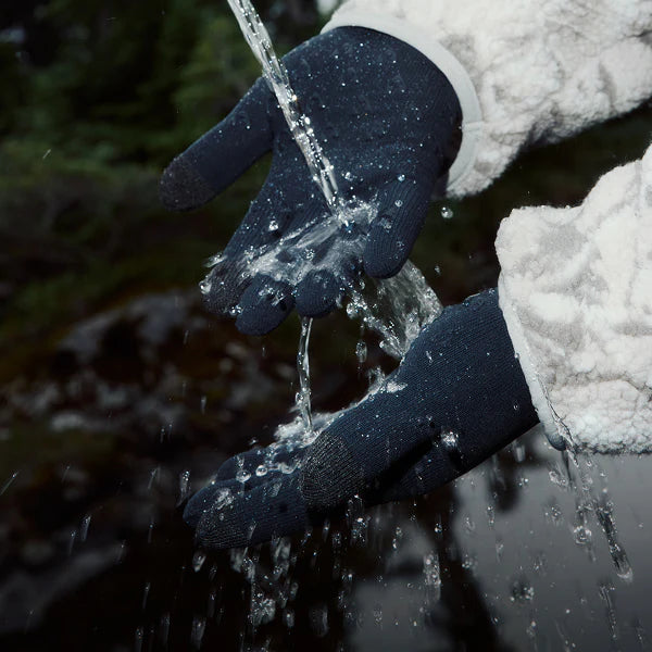 Person wearing gloves holding water from a stream in a snowy landscape