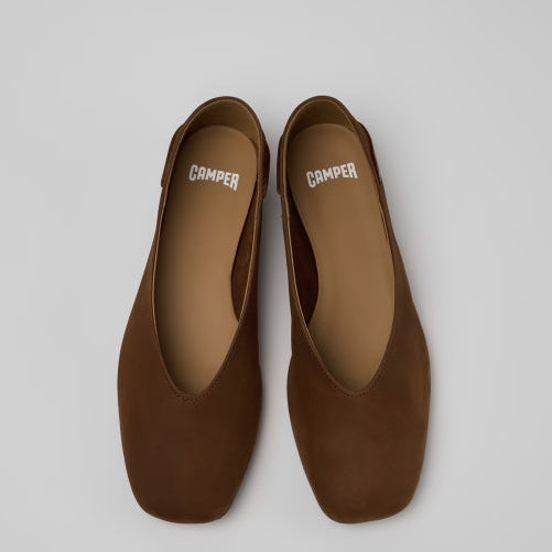 A pair of brown suede flat shoes with square toes, shown from a top-down view on a light gray background. The brand name 'CAMPER' is printed in white on the insole of each shoe.