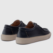 A pair of black leather low-top lace-up shoes with tan soles, shown from a three-quarters rear angle on a light gray background.