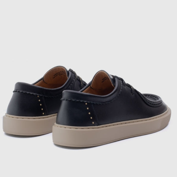 A pair of black leather low-top lace-up shoes with tan soles, shown from a three-quarters rear angle on a light gray background.