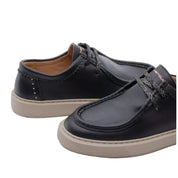 A pair of black leather boat shoes with beige soles and textured black-and-gold laces, shown on a light gray background.