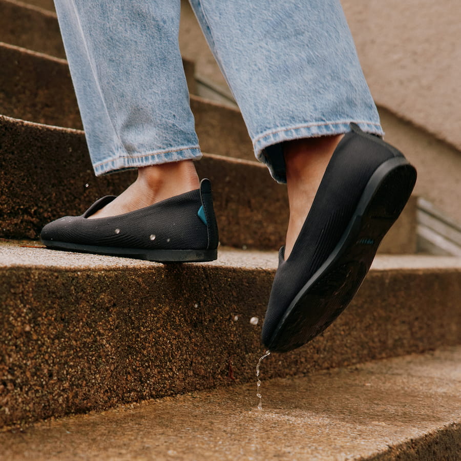 Person wearing black shoes and blue jeans stepping onto wet concrete steps.