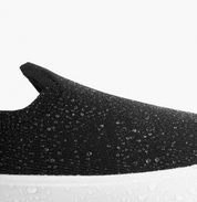 Close-up of a black slip-on sneaker with a white sole on a light gray background